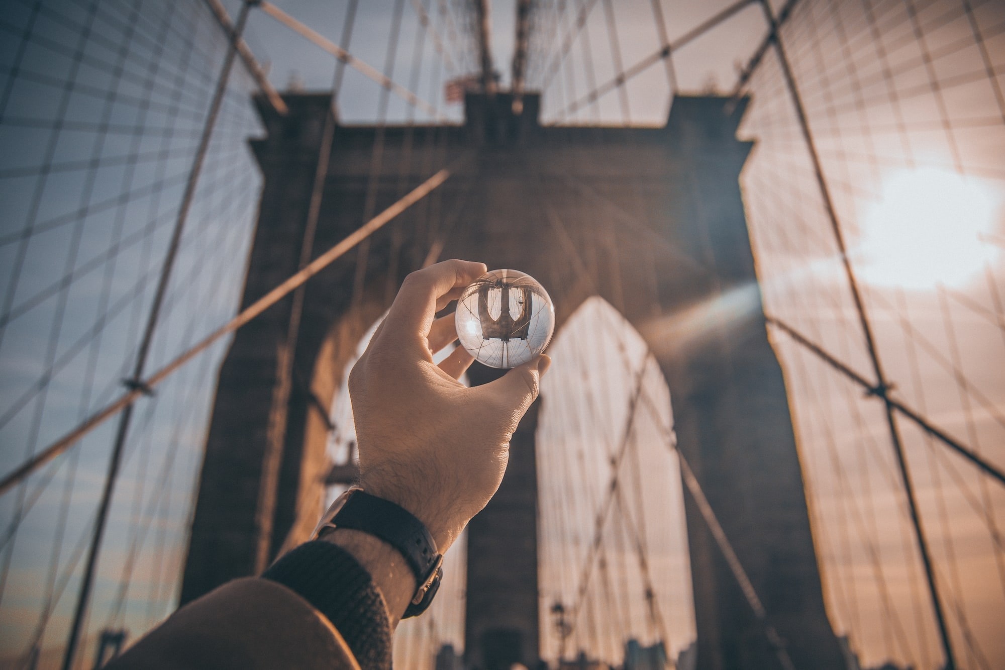 A glass ball is being held up to the arches of the Manhattan bridge. The upside down image can be seen in the ball representing perception.