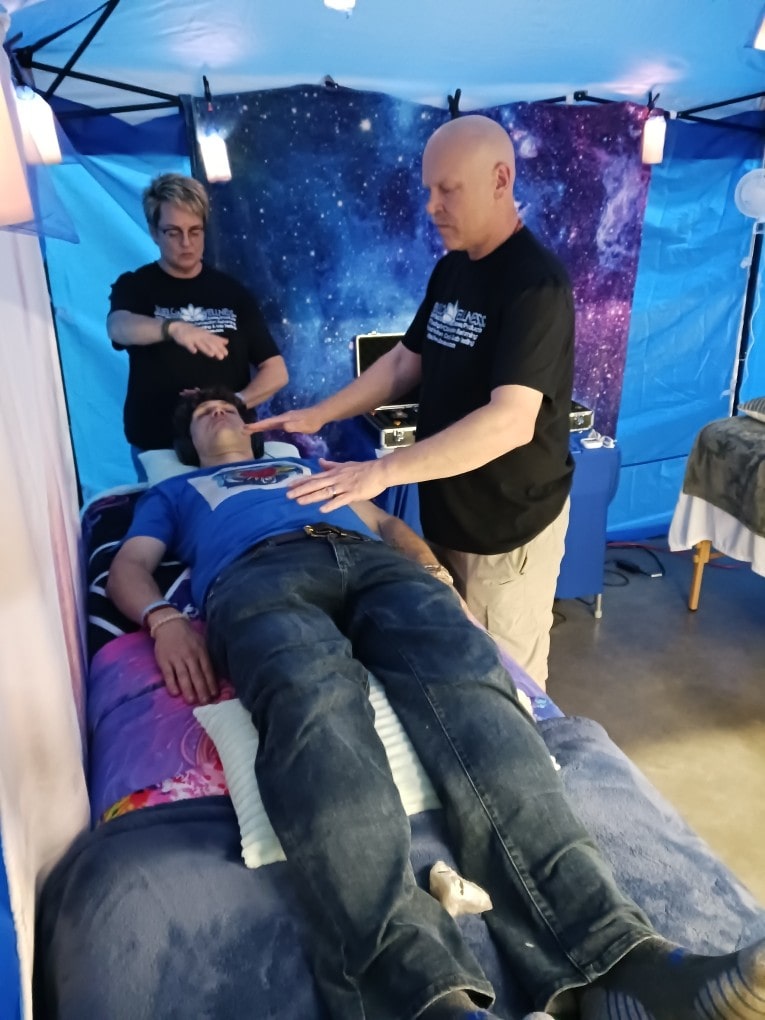 Frank and Julie are holding Reiki hand positions above a client during a session at a wellness fair.