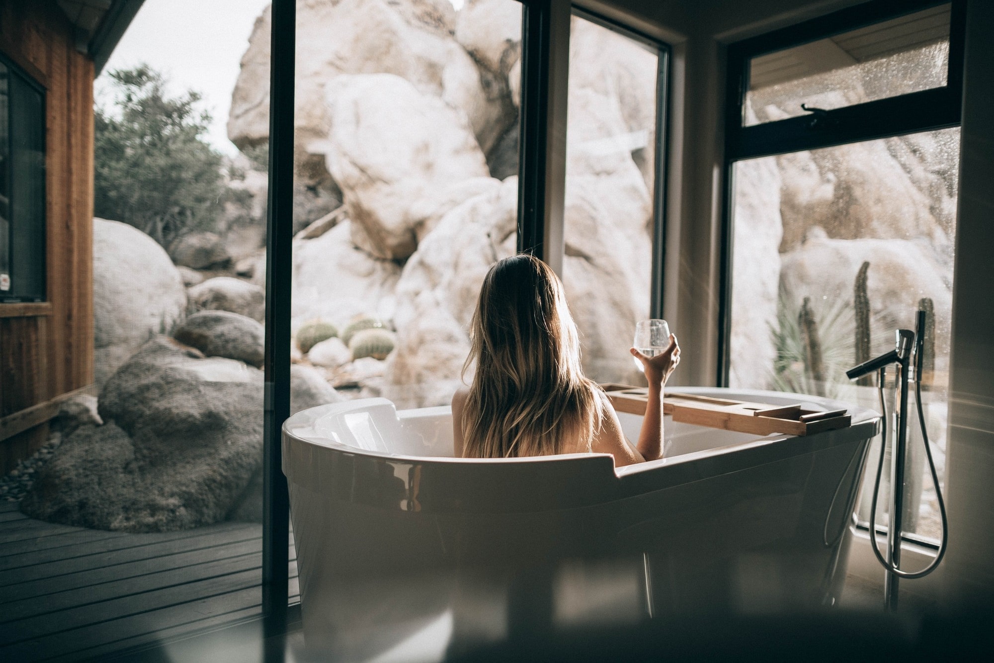 Woman relaxing in a deep soaker tub filled with Ancient Minerals magnesium salts with a glass in her hand.