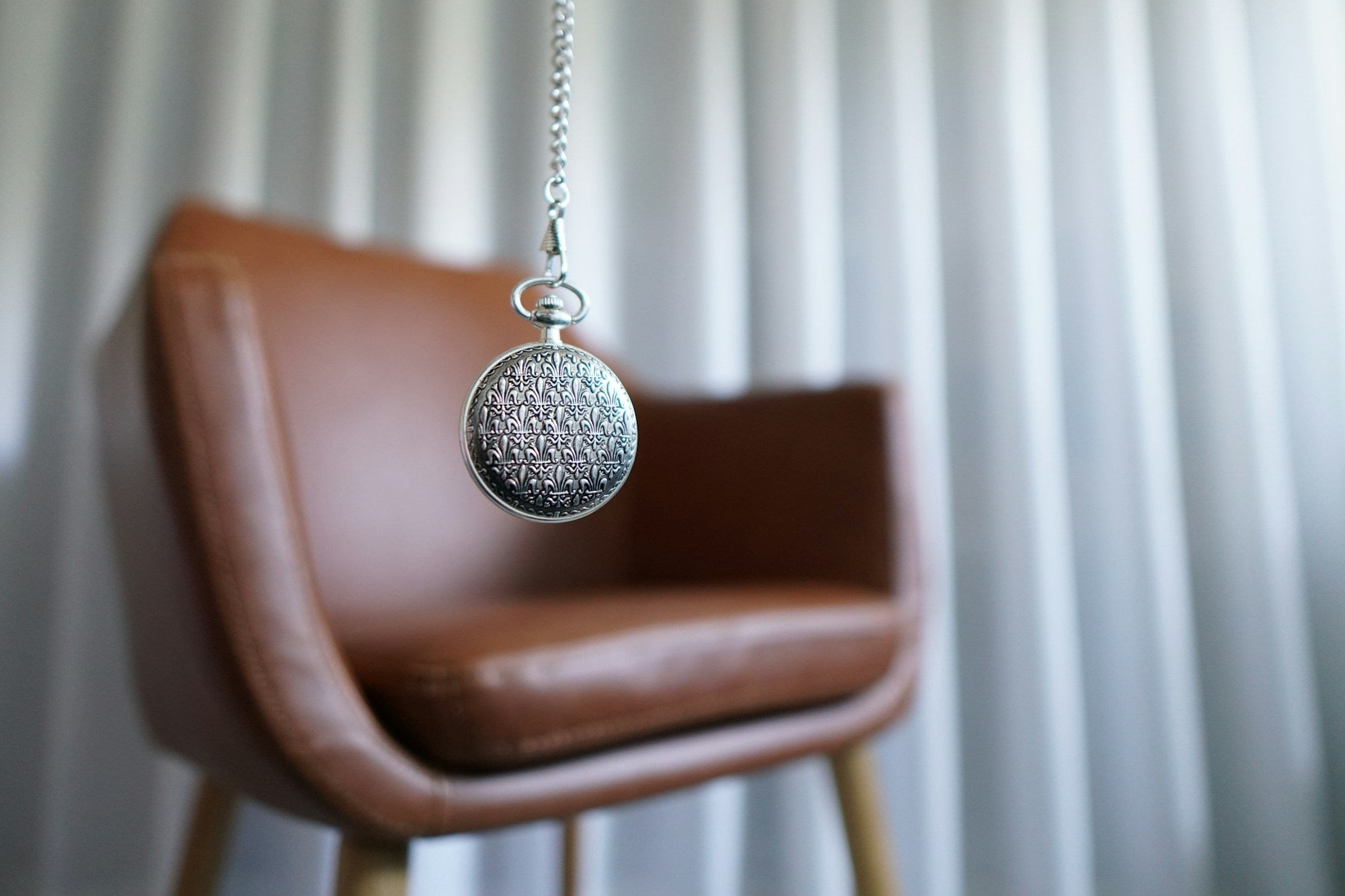 A pocket watch, in front of a comfortable leather chair, represents the hypnosis part of QHHT.